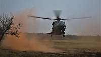 Ein Hubschrauber wirbelt beim Landevorgang roten Rauch auf, mit dem die Stelle markiert worden ist.