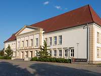 Sitz des Inspekteurs des Heeres in Strausberg Ein helles Gebäude mit rotem Dach, an der linken und rechten Seite des Eingangs je ein Nadelbaum
