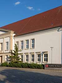 Sitz des Inspekteurs des Heeres in Strausberg Ein helles Gebäude mit rotem Dach, an der linken und rechten Seite des Eingangs je ein Nadelbaum