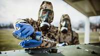 Ein Soldat in ABC-Schutzkleidung mit Kampfstoffspürpumpe an einer Flüssigkeit