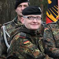 Ein Soldat mit schwarzem Barett und Brille schaut freundlich in die Kamera.