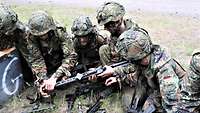 Sechs Soldaten sitzen bei der Waffenausbildung auf einer Wiese und zerlegen ein Maschinengewehr.