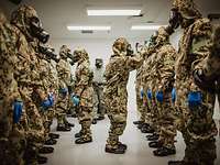 Soldaten in ABC-Schutzkleidung stehen sich gegenüber während zwei Soldaten die ABC-Masken überprüfen
