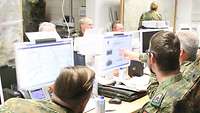Soldaten sitzen in zwei Reihen vor Computern. An den Wänden hängen zwei große Landkarten.