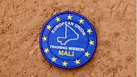 Das blaues Wappen der Europäischen Trainingsmission in Mali liegt auf sandigen Boden