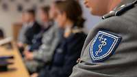 Wappen des Sanitätsdienstes an einer Uniformjacke, dahinter sind noch Soldaten unscharf zu sehen