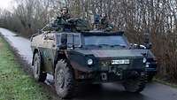 Ein Militärfahrzeug fährt auf einer Straße. Zwei Soldaten schauen aus den Luken heraus.