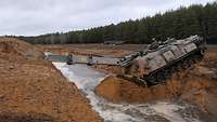 Ein Pionierpanzer fährt in einen Graben mit der Baggerschaufel als Unterstützung