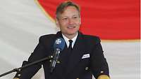 Ein Mann in Marineuniform steht vor einem Rednerpullt.