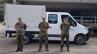 Drei Soldaten verschränken ihre Arme hinter dem Rücken und stehen vor einem weißen Transporter.