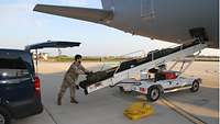 Ein Soldat legt einzelne Gepäckstücke auf ein Förderband, das diese dann zum Gepäckraum eines Flugzeugs transportiert