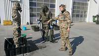 Zwei Soldaten in ABC-Schutzausstattung, eine Soldatin gibt Anweisungen 