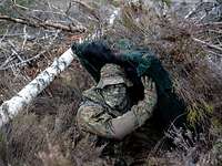Ein getarnter Soldat hebt zwischen Sträuchern und Büschen ein Platte über dem Kopf hoch.