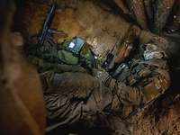 Ein Soldat sitzt gut getarnt unter der Erde in einer kleinen Höhle.