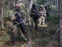 Mehrere Soldaten laufen hintereinander mit ihrer Ausrüstung durch den Wald.