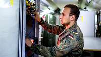 Ein Soldat steht vor einem Serverschrank und steckt Kabel um.
