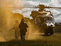 Drei Soldaten laufen im gelben Nebel auf einen am Boden wartenden Hubschrauber zu.