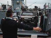 Ein Marinesoldat macht Handzeichen für den Fahrer eines Spähwagens, der auf ein Boot fährt.