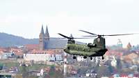 Ein großer Hubschrauber fliegt über Fritzlar, im Hintergrund der Dom der Stadt.