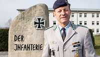 Soldat im Dienstanzug steht vor dem Stein der Infanterie und lächelt in die Kamera.