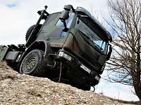 Ein grüner Lkw fährt im Gelände einen sandigen Hang hinunter. 