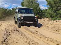 Ein grüner Geländewagen fährt auf einer Spur durch den beigen Zuckersand. 