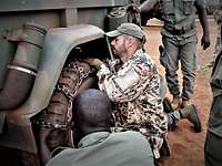 Ein Soldat zeigt drei Soldaten, die stehen, wie man eine Gleitschutzkette am Auto anlegt.
