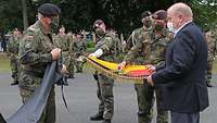 Soldaten und ein Zivilist falten eine Fahne, um sie in eine schwarze Hülle zu stecken, die ein anderer Soldat bereithält.