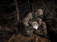 Ein Soldat in grüner Uniform gräbt bei Nacht mit seinem Klappspaten ein Loch in den beigen Sand.