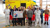 Frauen und Männer stehen vor einem Rettungswagen und halten das Zertifikat