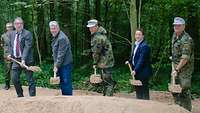 Drei Männer im Anzug und zwei in Uniform halten jeweils eine Schaufel mit Sand in der Hand, vor ihnen ein Sandberg.