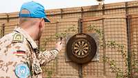 Ein Soldat hält einen Pfeil in der Hand und zielt damit auf eine Dartscheibe
