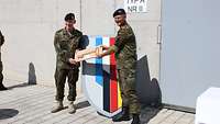 Zwei Männer in Uniform halten einen großen symbolischen Schlüssel in ihrer Mitte