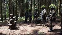 Soldaten stehen mit Helm und Maske im Wald. Sie hören einem Ausbilder zu.