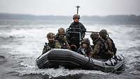 Mehrere Soldaten setzen mit einem Schlauchboot über. Vorn sichern zwei mit ihren Waffen die Fahrt.