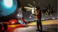 In der Nacht steht ein Pilot mit Sicherheitsweste am Flugzeug
