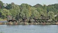 Kettenfahrzeug fährt auf einer Schwimmbrücke zum anderen Ufer.