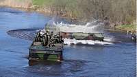 Soldaten fahren mit dem Motorboot 3 auf einem Gewässer zu einer Faltschwimmbrücke.