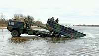Das Brückentransportfahrzeug steht auf einer Erhöhung im Wasser und lässt das Motorboot 3 zu Wasser.