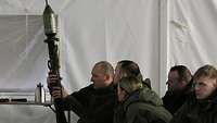 Eine Gruppe von Soldatinnen und Soldaten schaut sich die Patrone einer Panzerfaust an