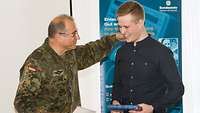 Ein Soldat überreicht einem Jugendlichen eine Urkunde. Er klopft dem jungen Mann auf die Schulter.