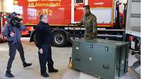 Soldat und zwei zivile Personen mit einer großen grünen Kiste der Bundeswehr, die gerade vom LKW entladen wurde.