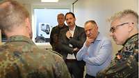 Drei Soldaten und zwei zivile Personen stehen in einer Halle bei einer Besprechung zusammen.