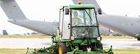 Ein Mann sitzt in einem Rasentraktor und mäht den Rasen auf einem Flugplatz