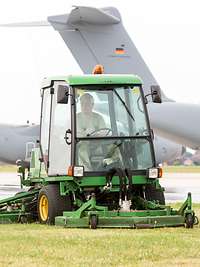 Ein Mann sitzt in einem Rasentraktor und mäht den Rasen auf einem Flugplatz