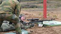 Ein norwegischer Soldat mit Gehörschutz redet mit einem am Boden liegenden deutschen Scharfschützen 