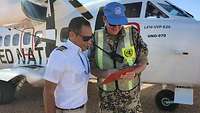 Ein Soldat steht neben einem Piloten vor einem Transportflugzeug. Beide schauen auf einen Zettel. 