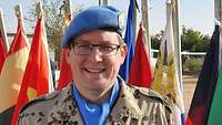 Ein Soldat mit blauen Barett steht vor den Flaggen verschiedener Nationen