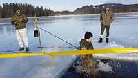 Zwei Soldaten sichern auf einem See einen Soldaten mit einem Seil, der in ein Wasserloch springt.