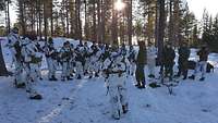 Eine Gruppe von Soldaten steht auf einer verschneiten Waldschneise, ein Soldat vor ihnen spricht.
